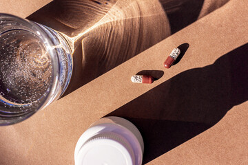 Pills and glass of water on brown background. Medicine, healthcare concept