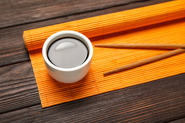 Bowl of soy sauce, chopsticks and bamboo mat on dark wooden background