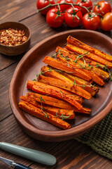 Plate with tasty baked carrots on wooden table, closeup