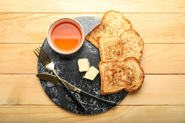 Board with toasts, butter and bowl of maple syrup on wooden background