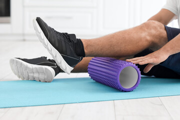 Young man training with foam roller at home, closeup