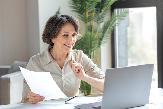 Smiling businesswoman having video meeting with employees or partners using laptop for remote work. Happy successful aged female communicates online sitting in the office