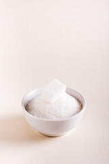 Fototapeta na wymiar Bowl with granulated sugar and a cube. Choosing between types of sugar. Vertical view