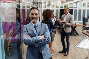 Portrait of mature businessman standing in modern office on colleagues background