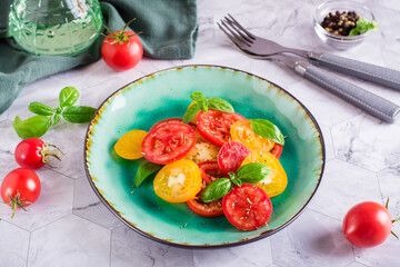 Fresh salad of yellow and red tomatoes with basil leaves on a plate on the table