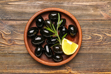 Plate with tasty black olives and piece of lemon on wooden background