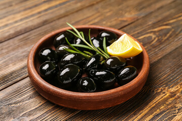 Plate with tasty black olives and piece of lemon on wooden background