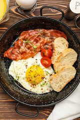 Frying pan with tasty fried egg, bacon and bread on wooden table, closeup