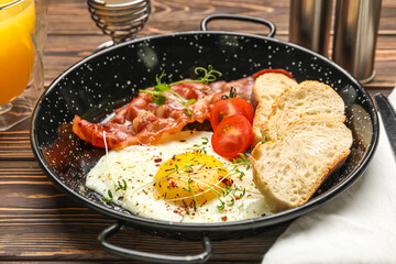 Frying pan with tasty fried egg, bacon and bread on wooden table, closeup