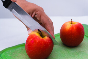 High quality photography. Close up of a person's hands with a knife cutting a red apple on an isolated white background.