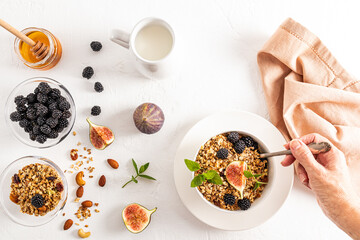 the hand of a young woman with a spoonful of muesli or granola filled during breakfast. a plate of...
