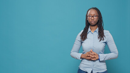 African american relaxed woman posing in front of studio camera, standing with hands crossed. Serious casual person with deep focused look feeling confident and successful over background.