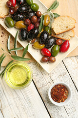 Composition with plate of delicious olives, spices and oil on light wooden background