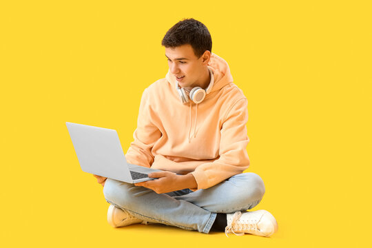 Teenage boy with headphones using laptop on yellow background