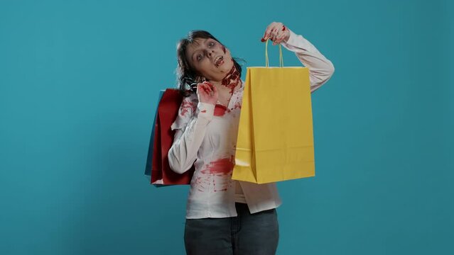 Undead mindless monster with colorful shopping bags from mall on blue background. Sinister looking mindless zombie with bloody and deep wounds and scars holding discounted store purchases.