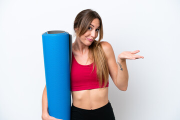 Young sport woman going to yoga classes while holding a mat isolated on white background having doubts while raising hands