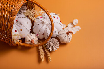 White decorative hand made pumpkins with shiny stones and pine cones in basket on colored background. Autumn harvest concept