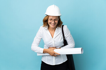 Young architect Georgian woman with helmet and holding blueprints over isolated background smiling a lot