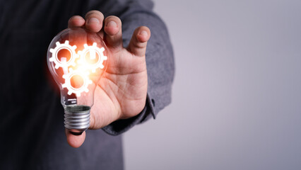 businessman Hand holding light bulb with cog gear glowing with orange light line and ray. Creative and new business knowledge thinking idea concept.