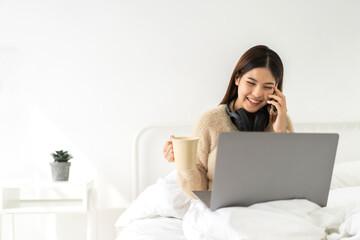 Fototapeta premium Young smiling happy beautiful asian woman work relaxing using laptop computer on sofa at home.Young creative girl working and use smartphone.work from home concept