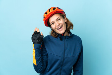 Young cyclist woman isolated on blue background saluting with hand with happy expression