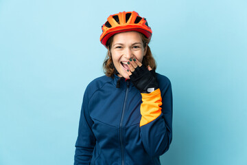 Young cyclist woman isolated on blue background happy and smiling covering mouth with hand