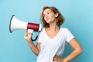 Young Georgian woman isolated on blue background holding a megaphone and thinking