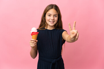 Child with a cornet ice cream over isolated pink background smiling and showing victory sign