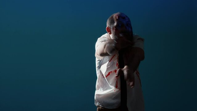 Scary brain-eating monster standing on blue background. Sinister aggressive looking mindless zombie with bloody and deep scars and wounds deranged by flashing lights. Studio shot