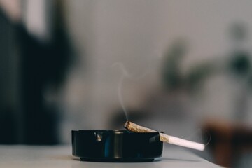 Shallow focus of a cigarette on an ashtray with a fading wisp of smoke