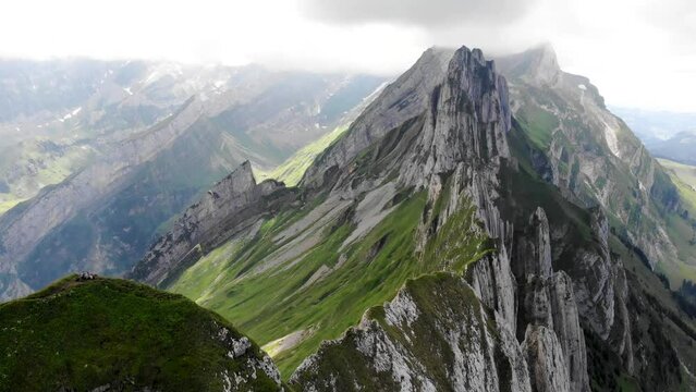 Aerial flyover over the side of Schafler ridge in Appenzell, Switzerland with cliffs, mountain peaks and lush summer green mountainside in view