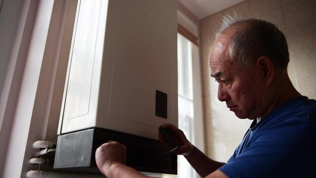 A senior man turning down the hot water boiler to save money trying to cope with dramatic increase in energy cost.