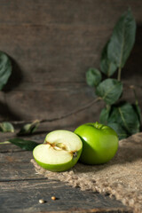 Green apple whole and cut half with leaves on burlap on wooden planks