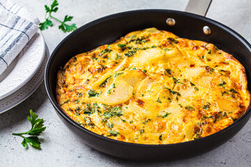 Traditional Spanish potato tortilla or omelette in black pan.
