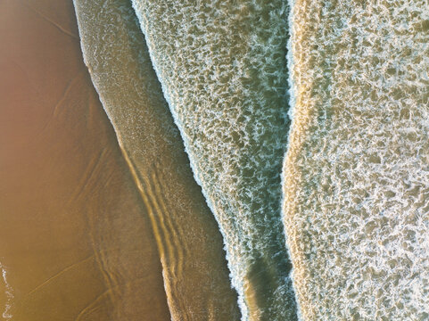 An aerial view of the wide beach and waves. Seascape from a drone during sunset. A sandy seashore. The sea and the shore. View of the beach from above.