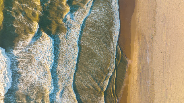 An aerial view of the wide beach and waves. Seascape from a drone during sunset. A sandy seashore. The sea and the shore. View of the beach from above.