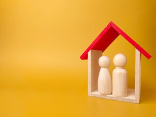 Two wooden figures inside wooden house on yellow background with copy space - insurance concept