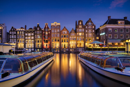 Damrak, Amsterdam, Netherlands. View of houses and boats during sunset. The famous Dutch canals and boats. A cityscape in the evening. Travel photography.