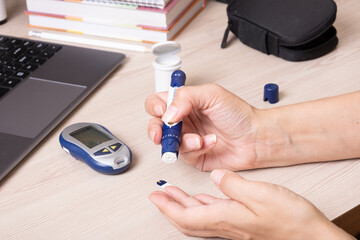 Female hands with a glucometer at the desk. The lifestyle of a person with diabetes, measuring the level of glucose