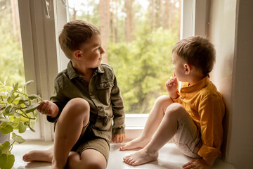 Children sitting on windowsill and waiting for someone comming. Two brothers, friends. Cute...