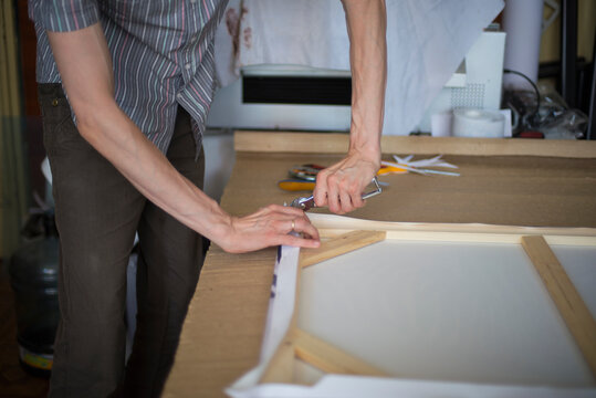 close up of a person hands stretching the canvas on the stretcher