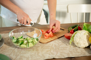 Obraz na płótnie Canvas A pregnant woman cuts vegetables into a salad in the kitchen.