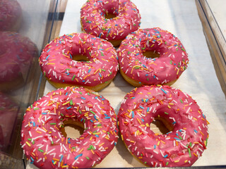 Pink frosted doughnuts with colorful sprinkles, close-up. Storefront in the bakery department.