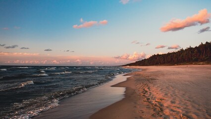 Landscape view of the Baltic sea with a sandy beach and an orange-colored sunset in the background - obrazy, fototapety, plakaty