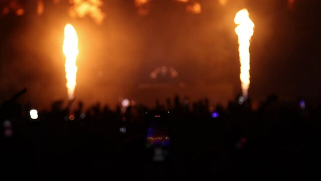 Open-air concert stage at night with fans dancing at a concert or festival party in front of bright stage lights, slow motion