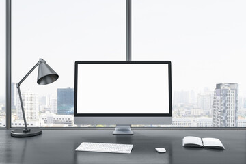 Close up of blank white computer screen on gray office desktop with objects, lamp and supplies on panoramic window and city view background. Mock up, 3D Rendering.