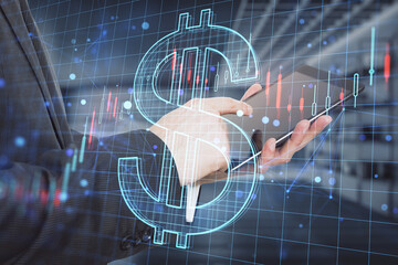 businessman hand pointing at tablet with creative glowing dollar sign hologram with forex chart on blurry office interior background. 