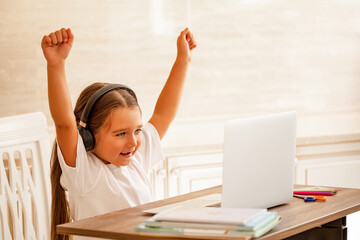 Smiling little caucasian girl having video call in remote classroom with teacher using laptop at desk at home, happy little kid greeting with tutor, learning online on computer, home learning concept 