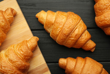 Freshly baked croissants on wooden cutting board on black background.