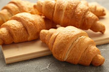 Freshly baked croissants on wooden cutting board on grey background.